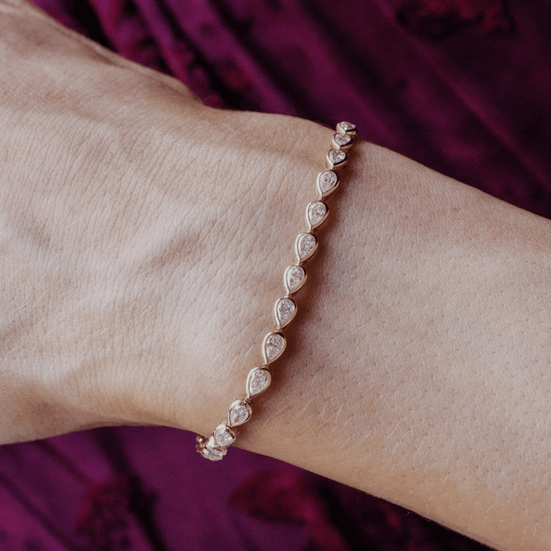 14k gold pear cut, lab grown diamond tennis bracelet featured on the wrist of a model. 