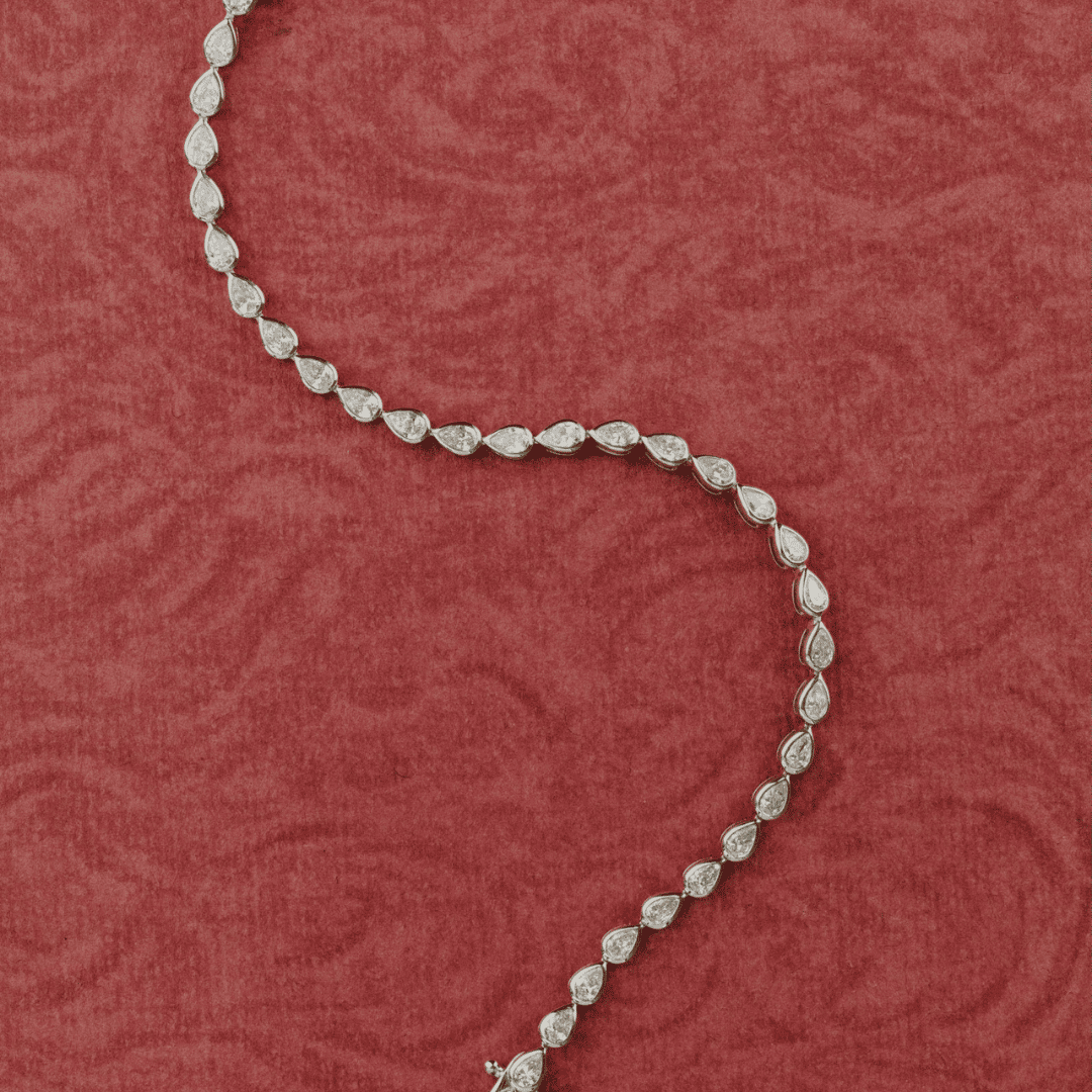 14k gold pear cut, lab grown diamond tennis bracelet featured on a textured red surface.  