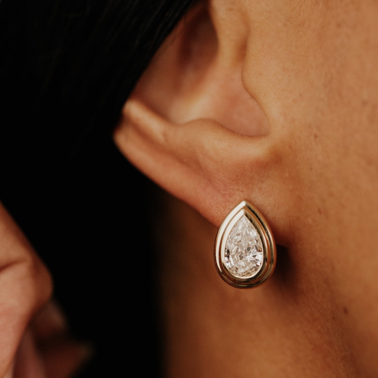 Pear-shaped lab grown diamond earring worn by a person with a blurred background.