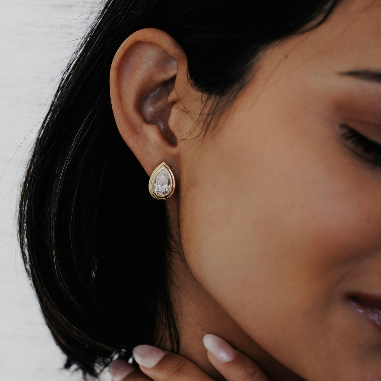 Close-up of a woman wearing a pear-shaped lab grown diamond earring with a blurred background.