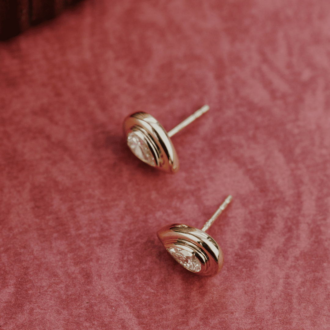 14k gold lab grown diamond earrings showcased on a textured red surface showing the side of the earring. 