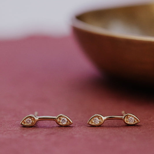 Gold stud earrings with small diamonds on a curbed bar a red surface.