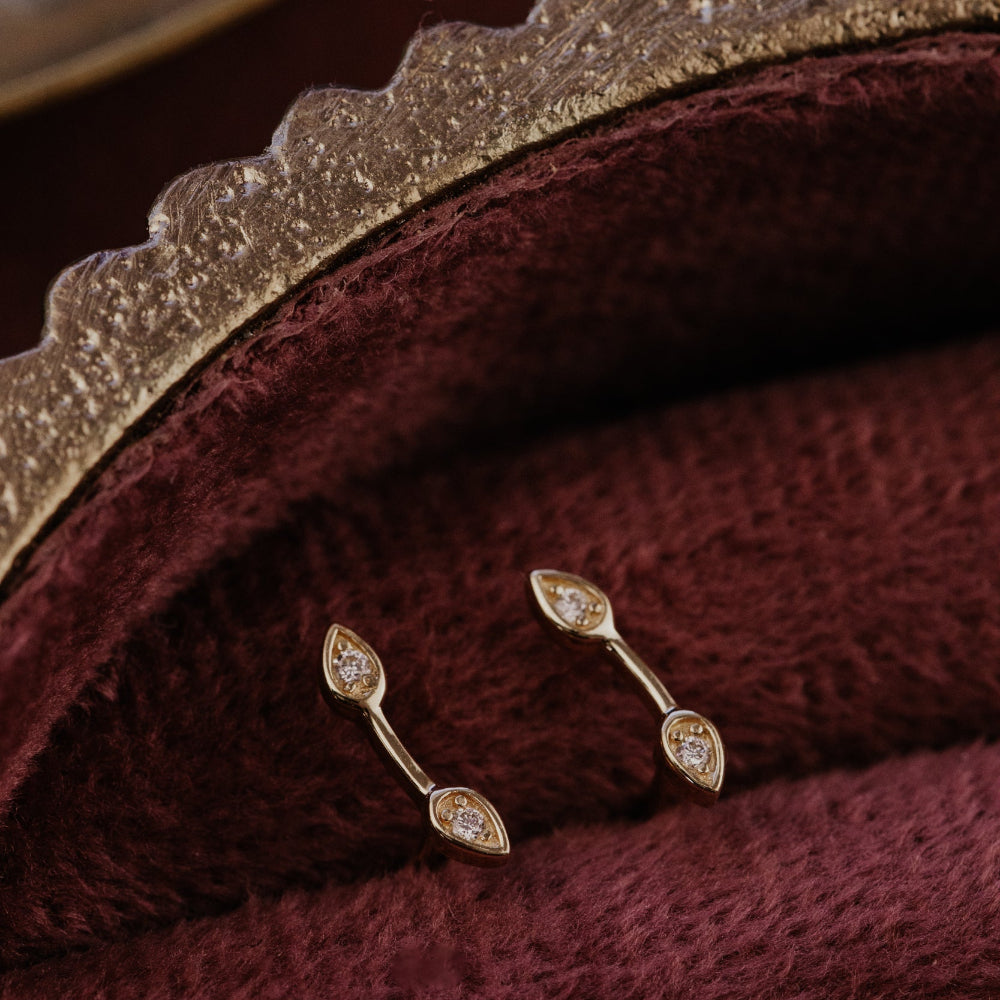 Gold earrings with diamonds on a burgundy fabric background.