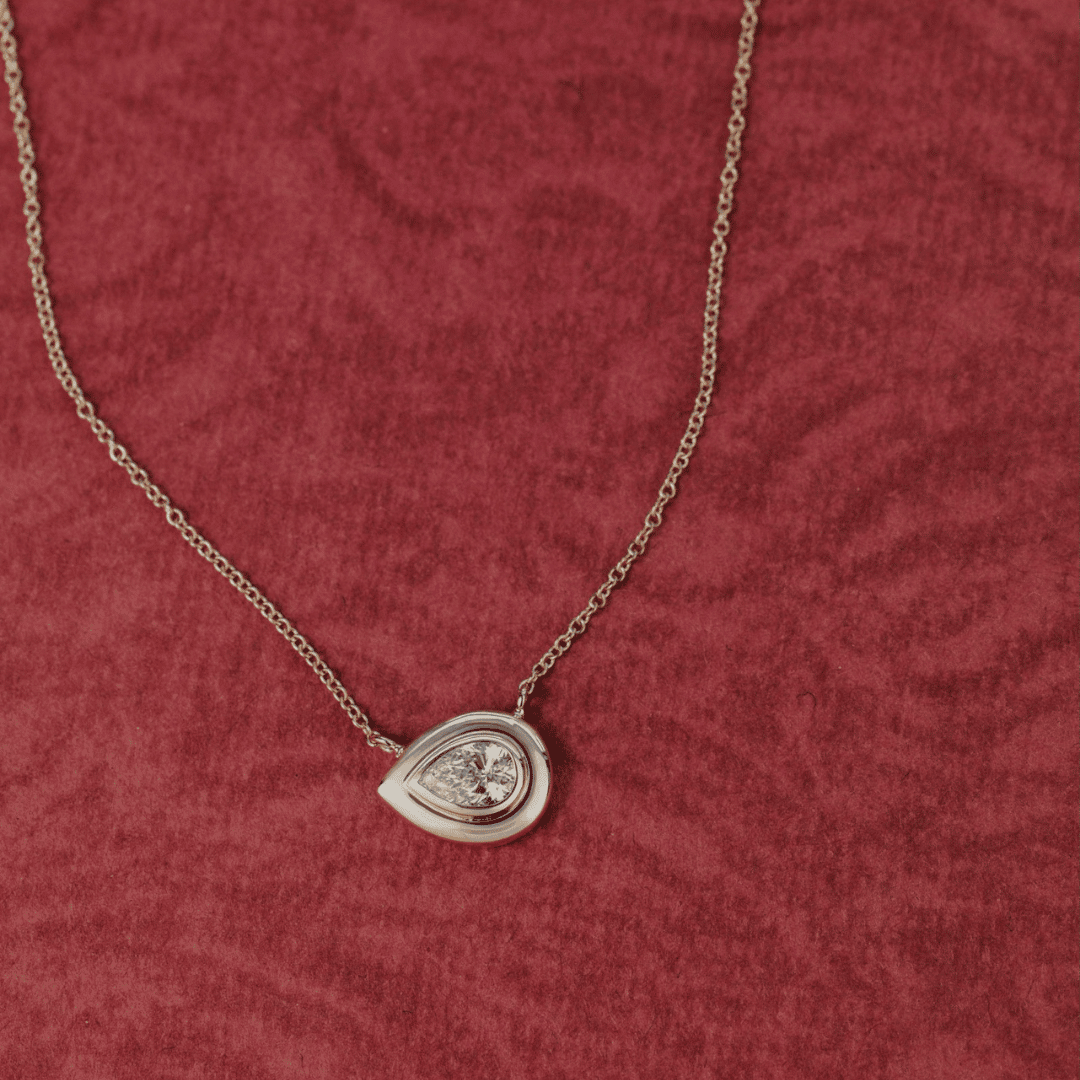 14k gold pear cut, lab grown diamond chain necklace showcased on a red textured surface. 