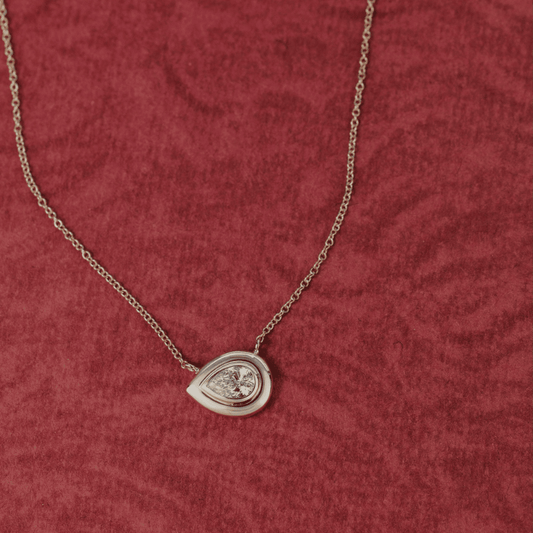 14k gold pear cut, lab grown diamond chain necklace showcased on a red textured surface. 