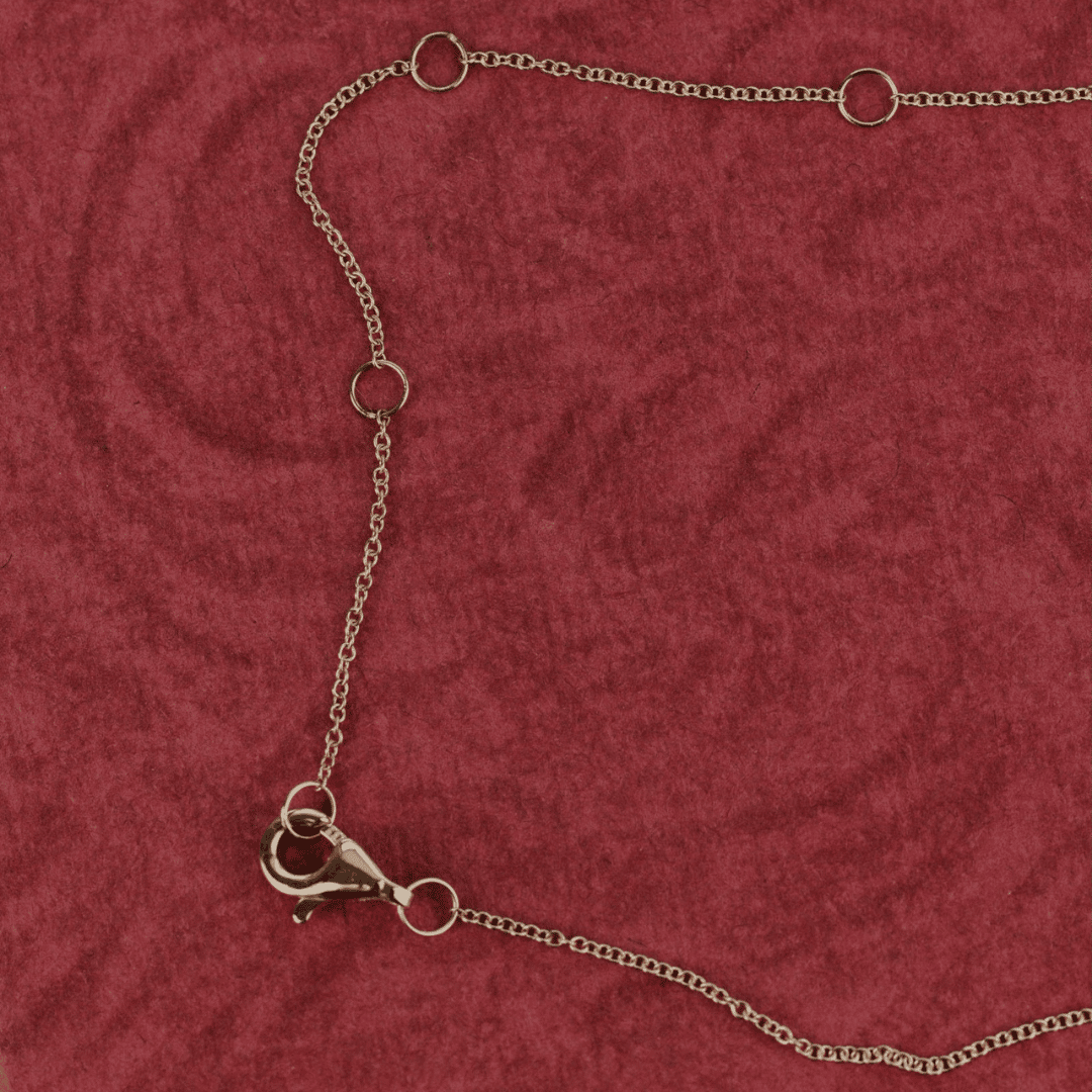 14k gold pear cut, lab grown diamond chain necklace showcased on a red textured surface showing the clasp. 