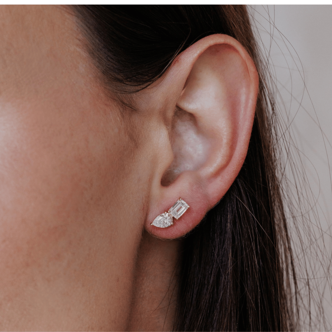 14k gold diamond earrings emerald and pear shaped set in prongs showcased in the ear of a model. 