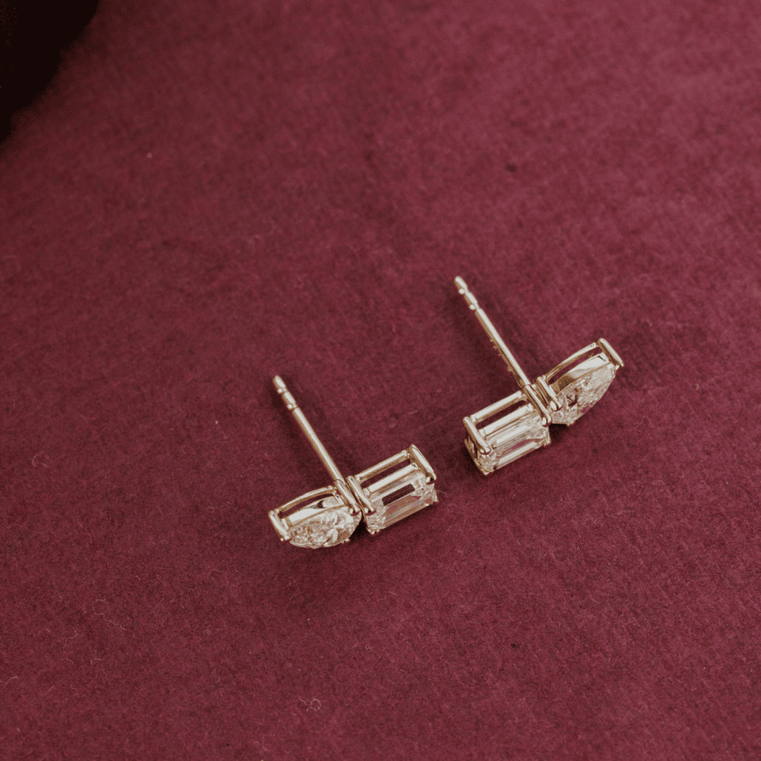 14k gold diamond earrings emerald and pear shaped set in prongs showcased on a textured red surface. 