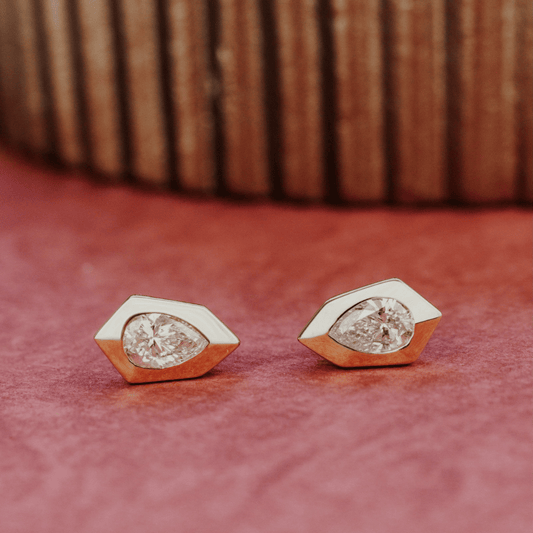 14k gold, pear-shaped diamond earrings set in prongs showcased on a textured red surface. 