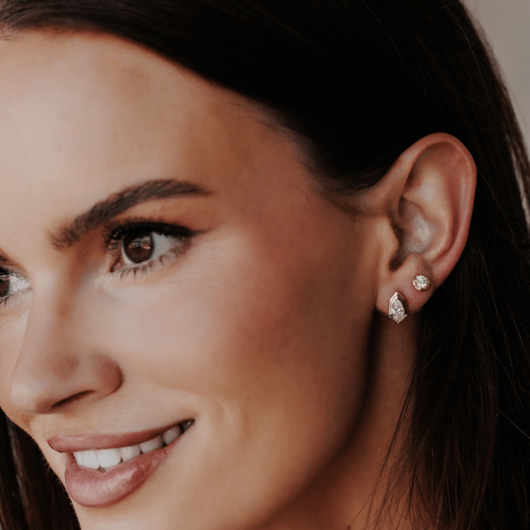 14k gold, pear-shaped diamond earrings set in prongs showcased in the ear of a model. 