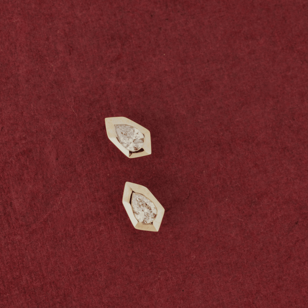 14k gold, pear-shaped diamond earrings set in prongs showcased on a textured red surface. 