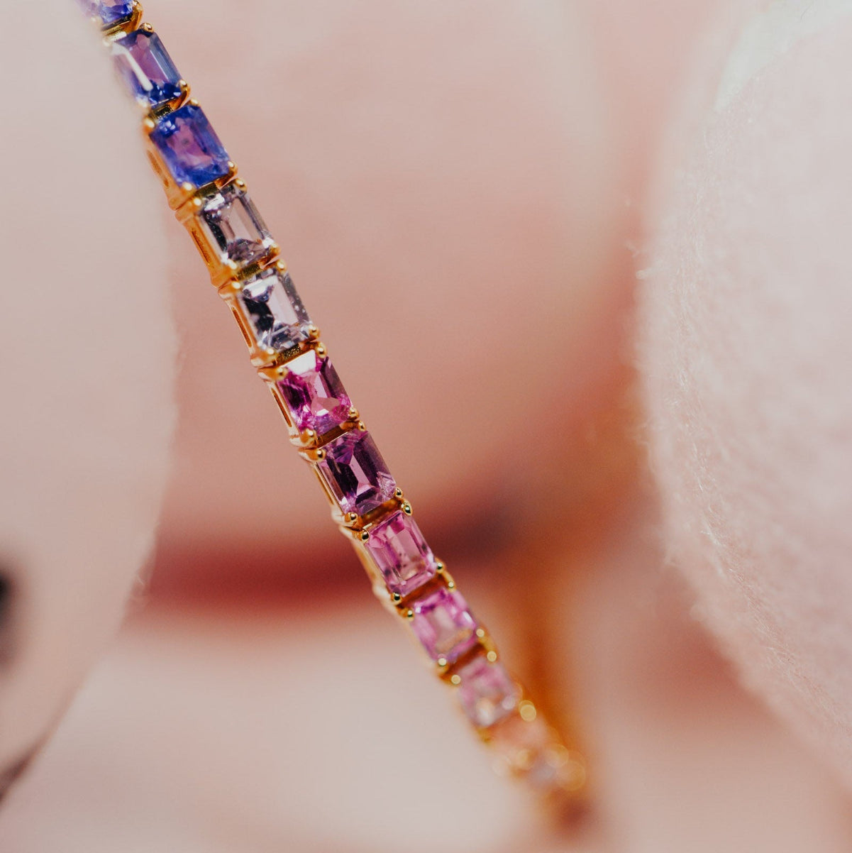 Close-up detail of the Rainbow Emerald Cut Sapphire Tennis Bracelet in 14k yellow gold, highlighting the graduated blue, lavender, and pink natural sapphires in prong settings.

