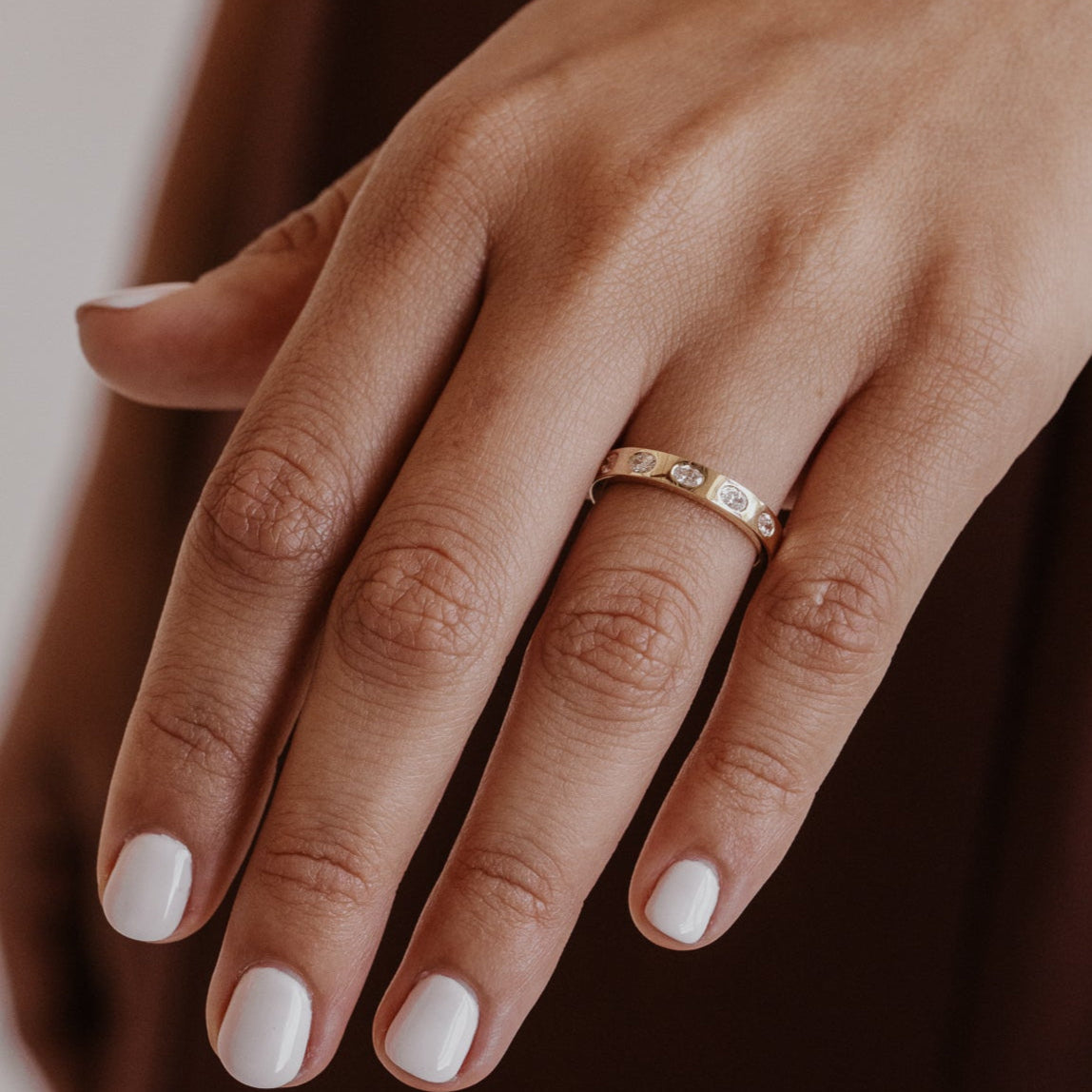 Close-up of a hand wearing a gold wedding band with oval diamonds with a blurred background