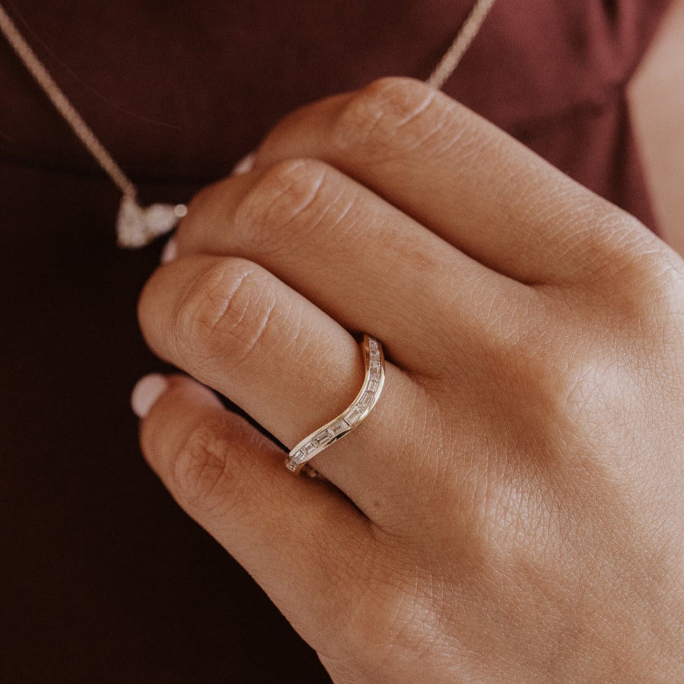 Close-up of a hand wearing a gold curved wedding band with diamond accents with a blurred background