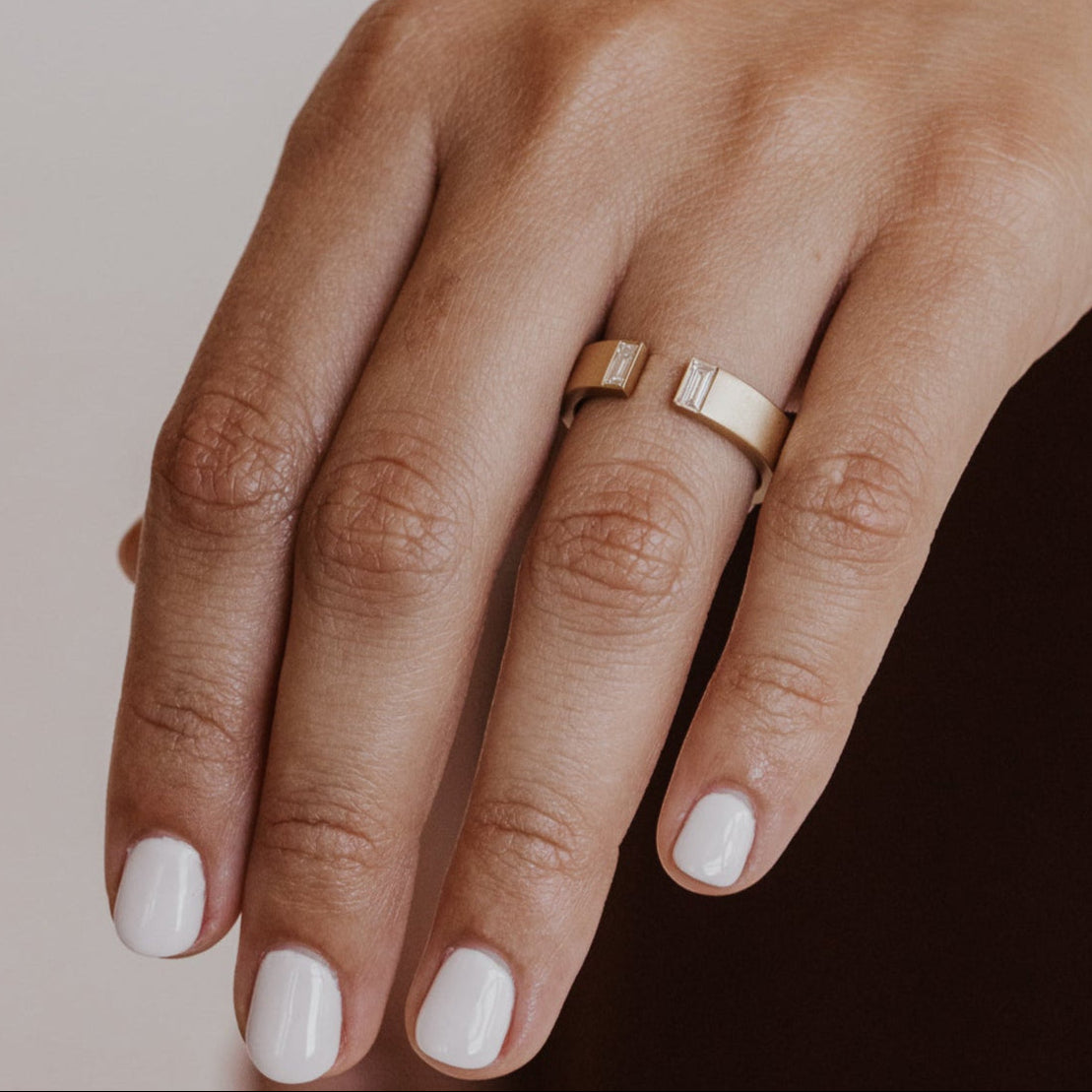 Close-up of a hand wearing a gold band with a neutral background