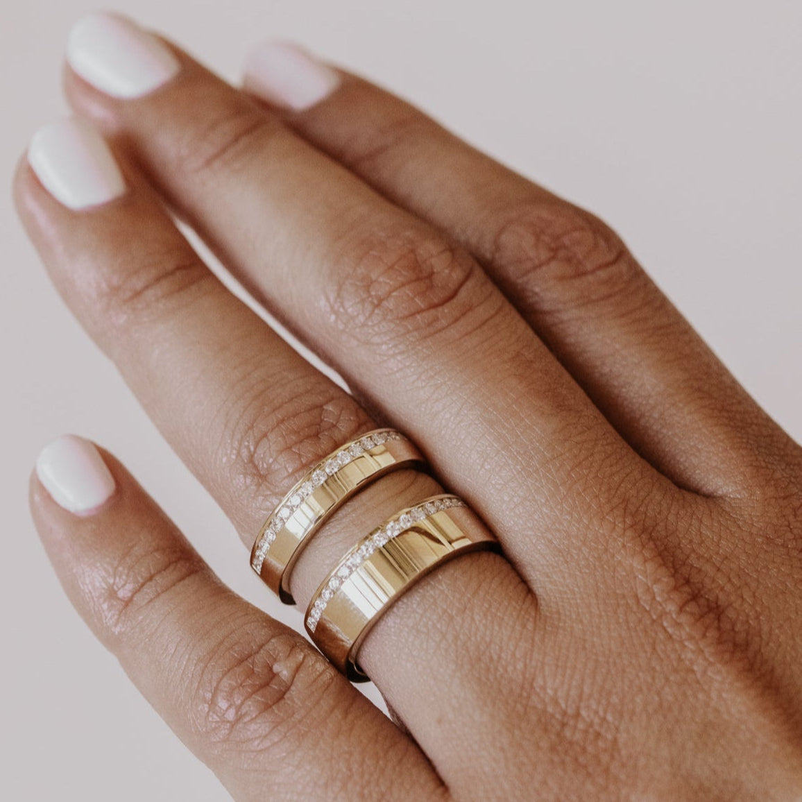 Hand wearing two gold rings with a plain background