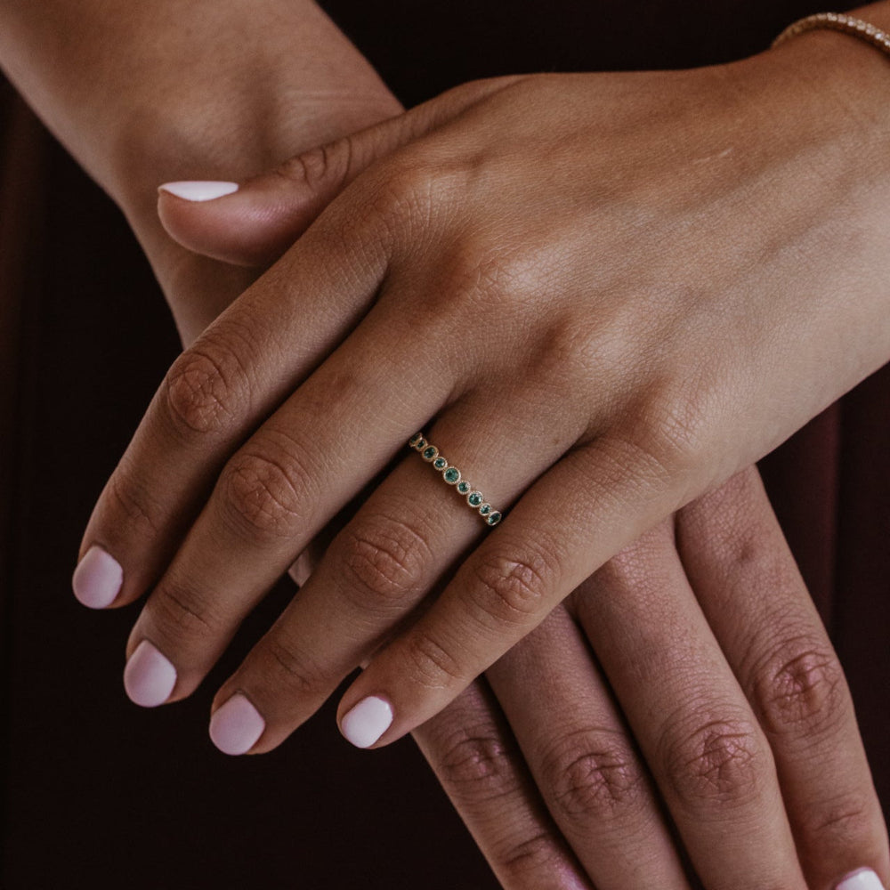 Close-up of a hand wearing a ring with green emerald gemstones on a dark background