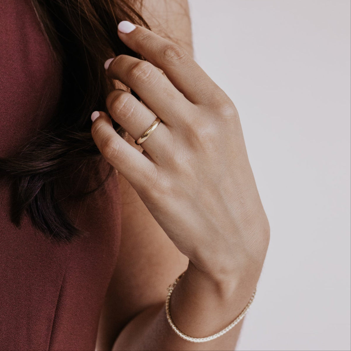 Close-up of a hand with a gold ring and bracelet, touching hair against a neutral background