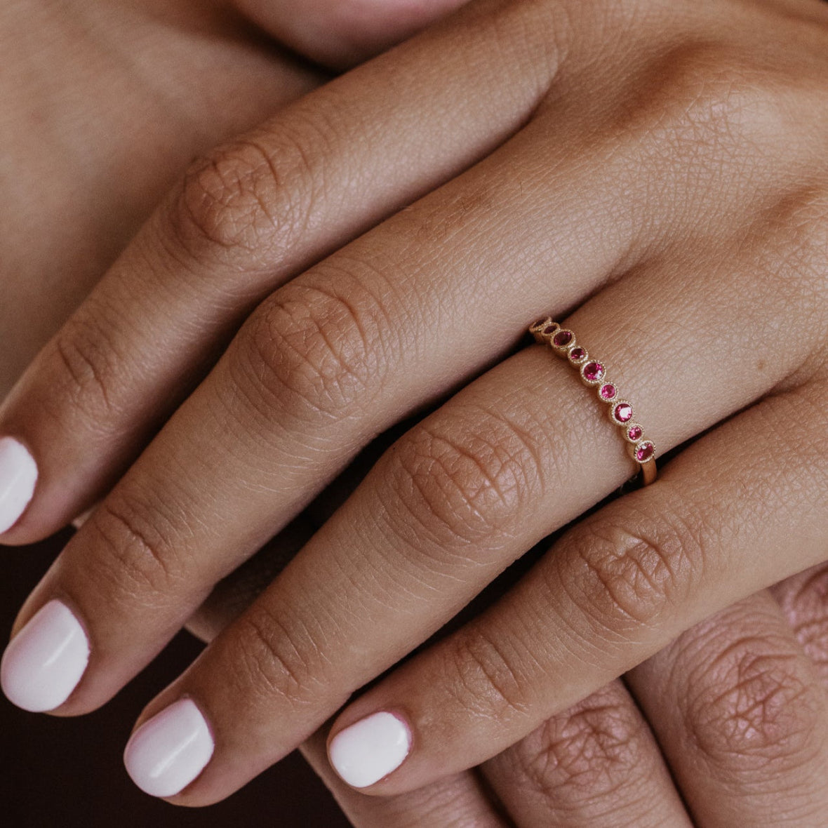 Close-up of a hand wearing a red ruby gemstone wedding band on a dark background