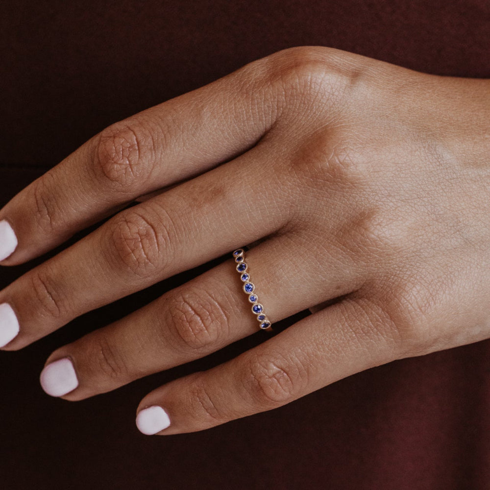 Hand wearing a white gold wedding band with blue sapphires  on a dark background