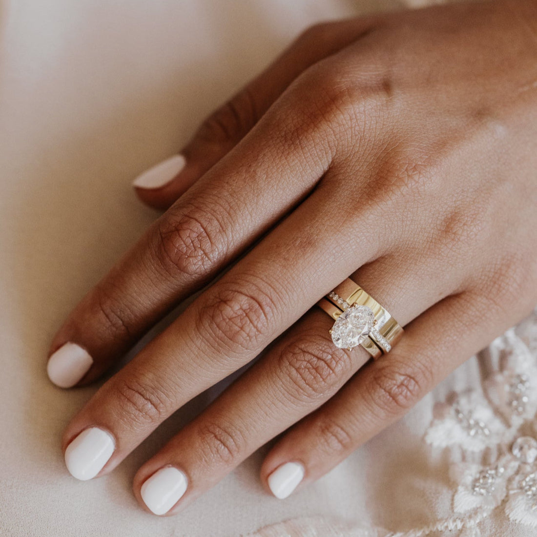 Hand wearing a gold ring with a diamond on a soft, neutral background