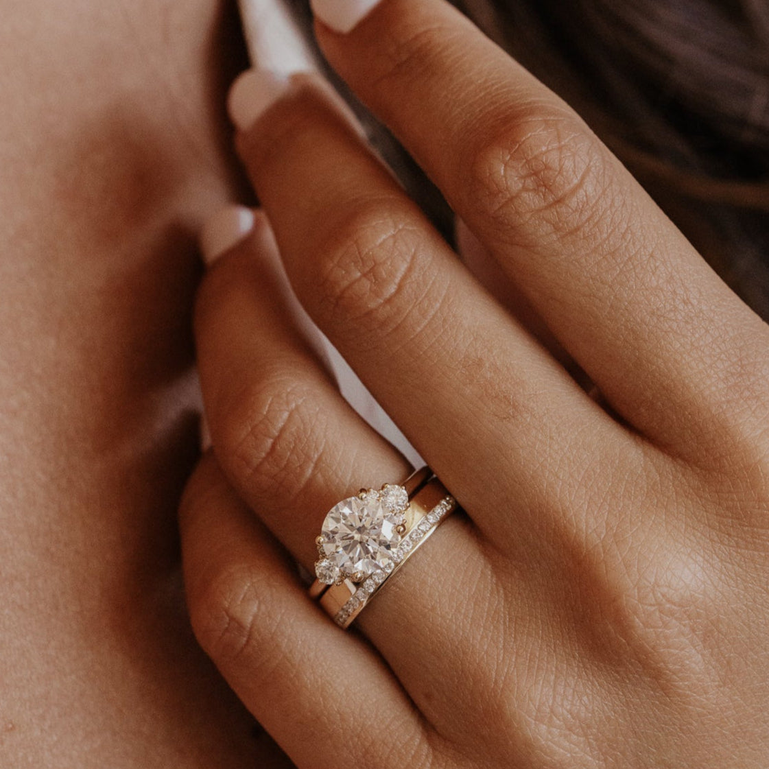 Close-up of a hand wearing a diamond ring with gold diamond wedding band a blurred background