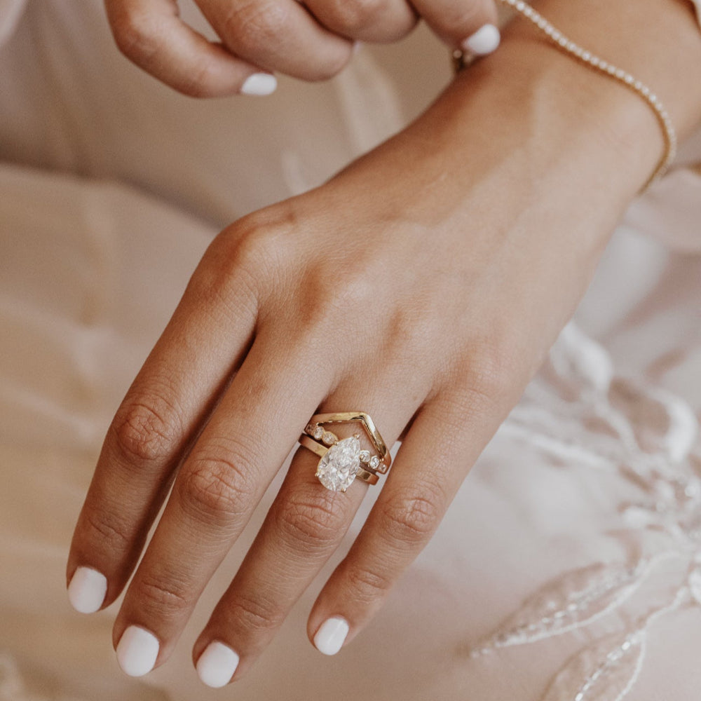 Close-up of a hand wearing a pear diamond ring with a gold v wedding band soft background