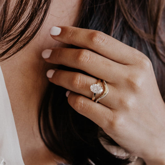 Close-up of a hand wearing a pave diamond wedding with a oval diamond engagement ring with a blurred background
