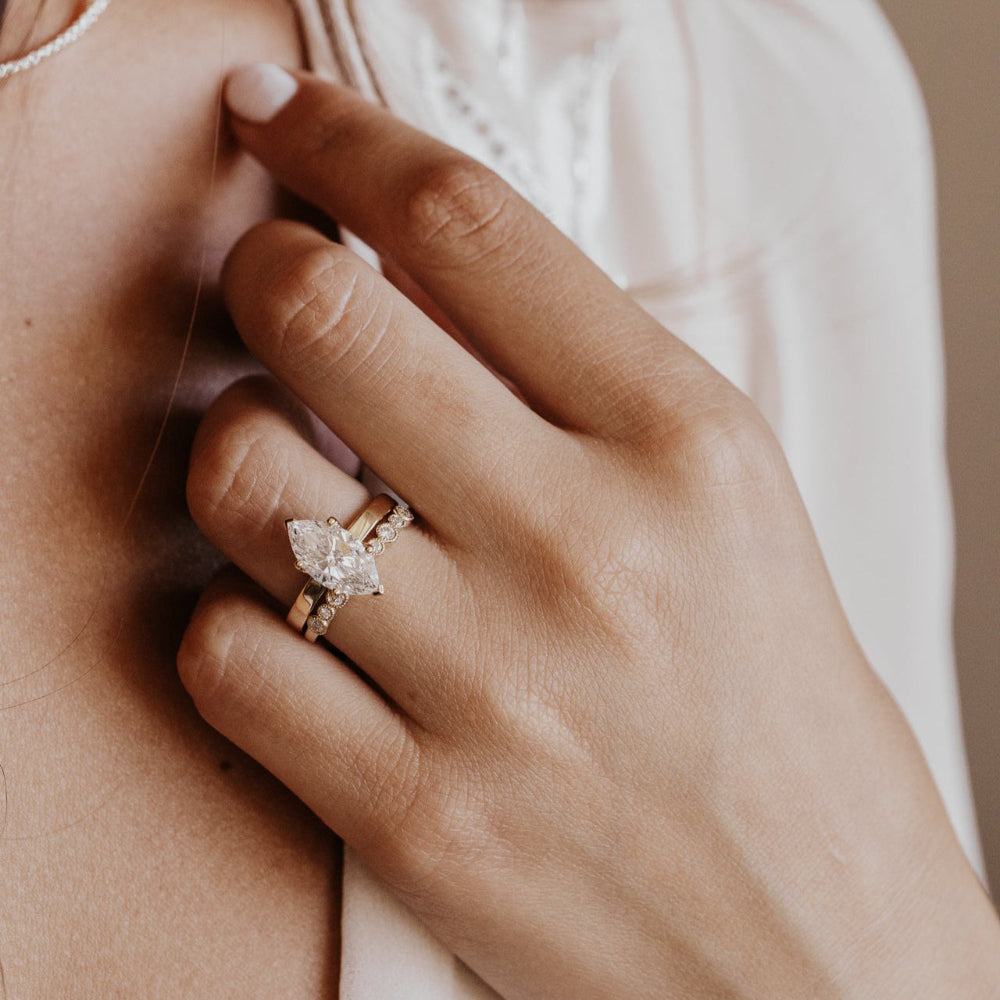 Close-up of a hand wearing a marquise diamond engagement ring with a soft background