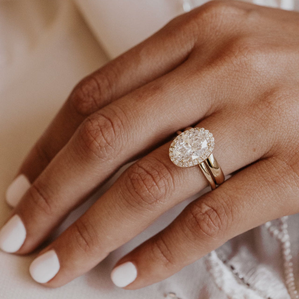 Close-up of a hand wearing a diamond ring paired with a gold wedding band with a soft background