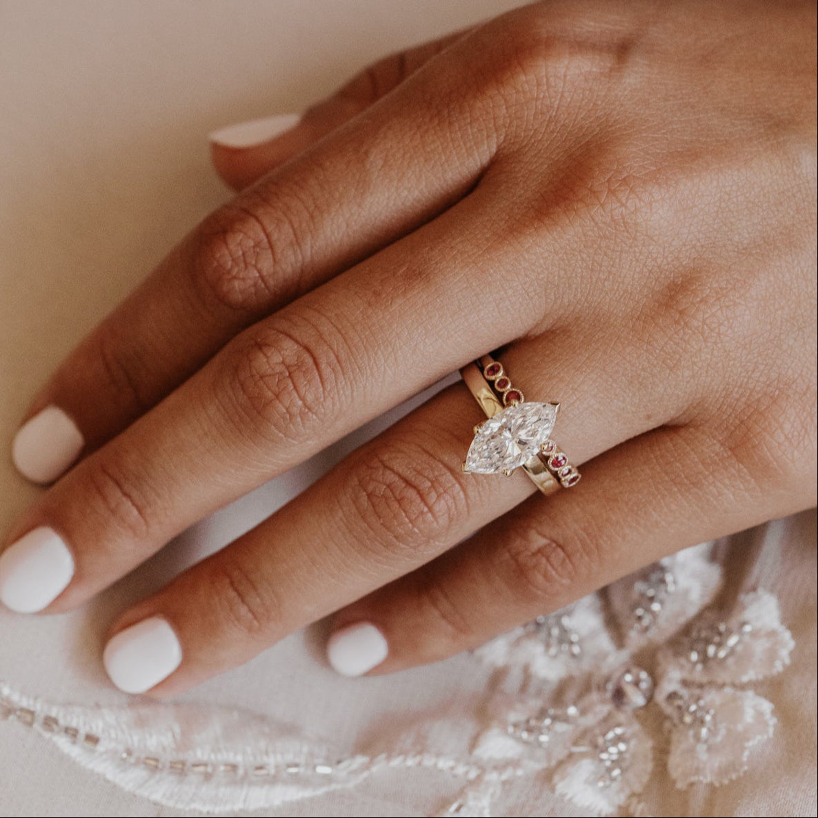 Close-up of a hand wearing a pear diamond engagement ring paired with a ruby wedding band on a textured fabric background