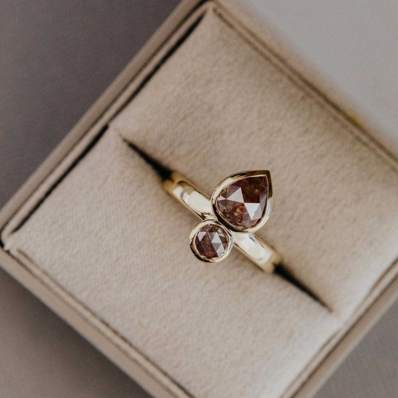 Gold Reese ring with two rustic diamonds in a beige jewelry box.