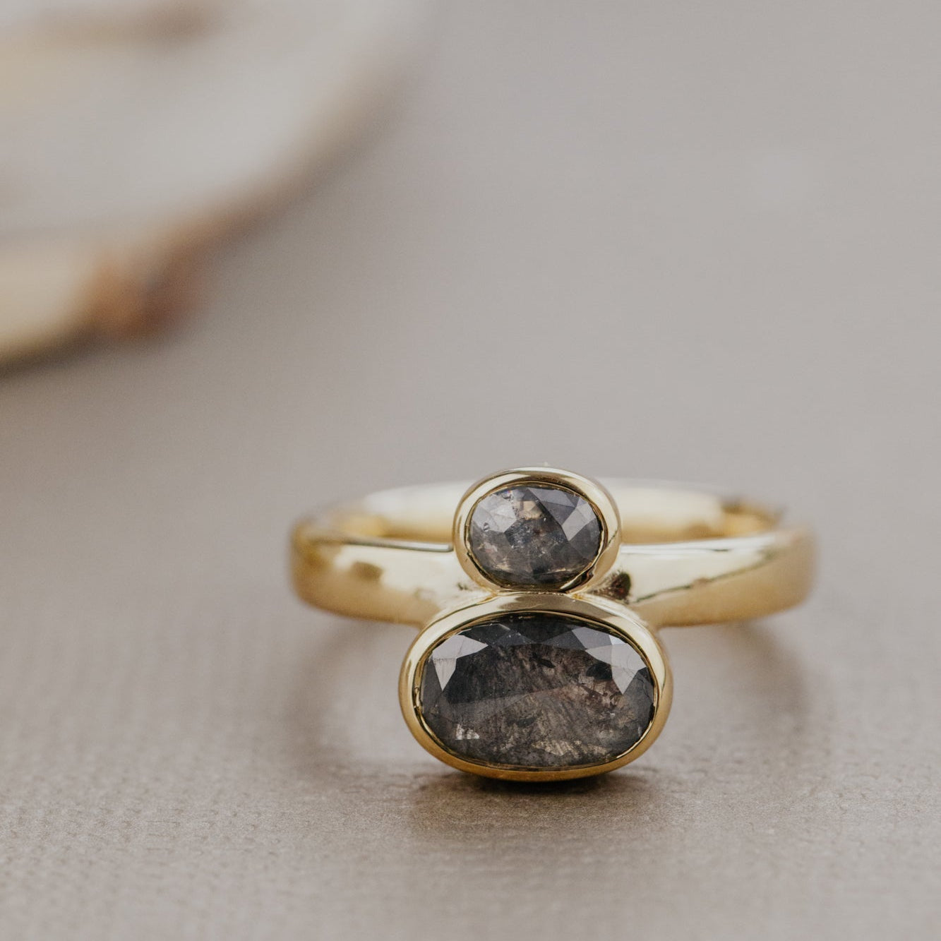 Gold ring with two dark rustic diamond gemstones on a neutral background.