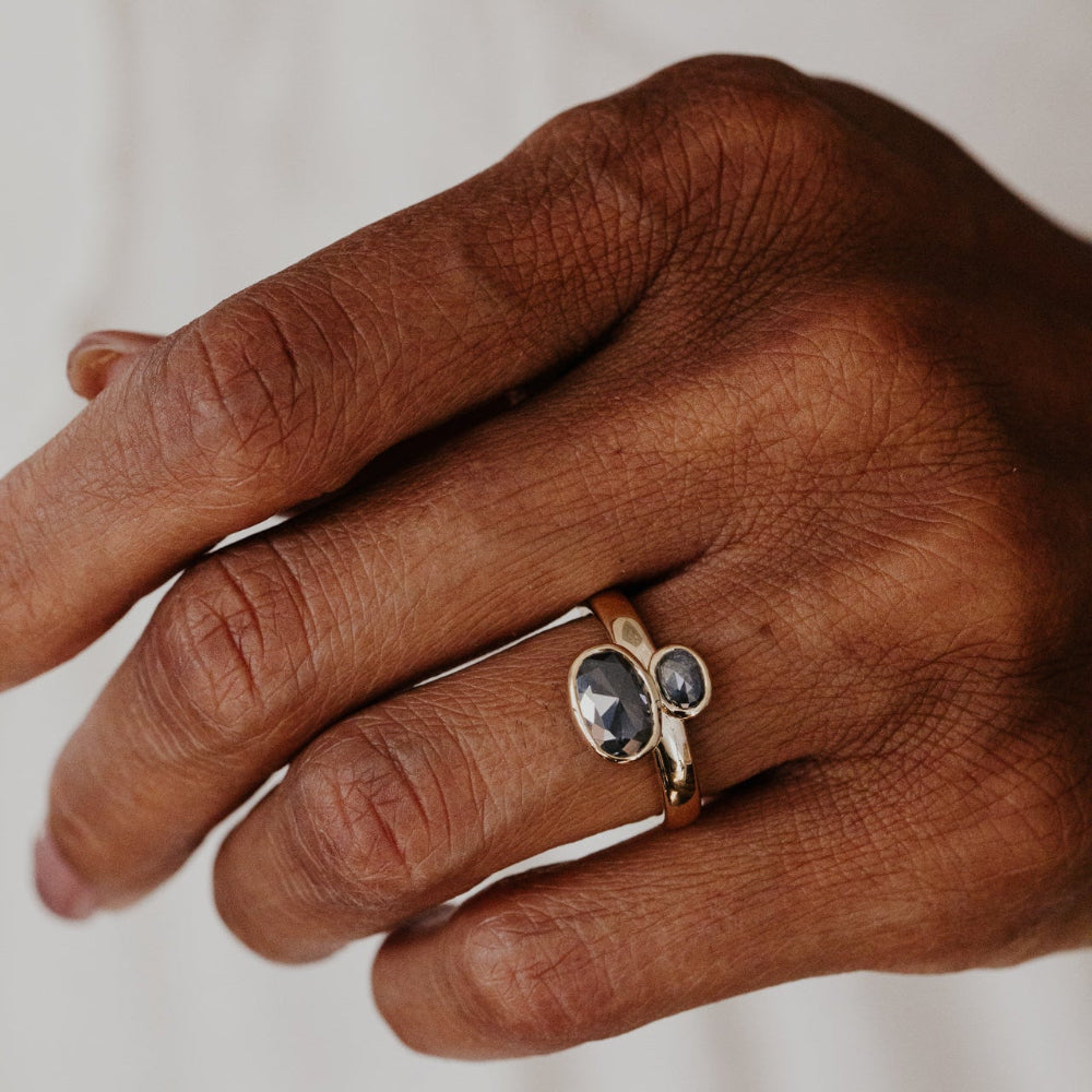 Hand wearing a gold ring with a rustic diamond gemstone on a neutral background.