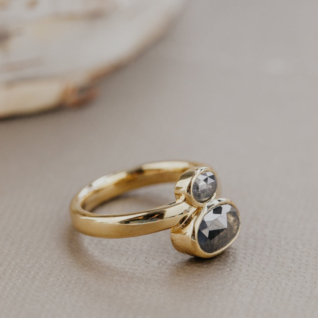 Gold ring with two rustic diamond gemstones on a neutral background.