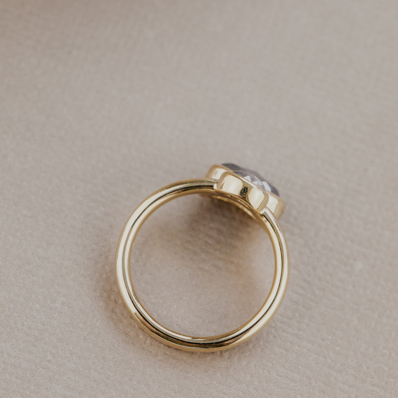 Gold ring with a rustic diamond gemstone on a beige surface.