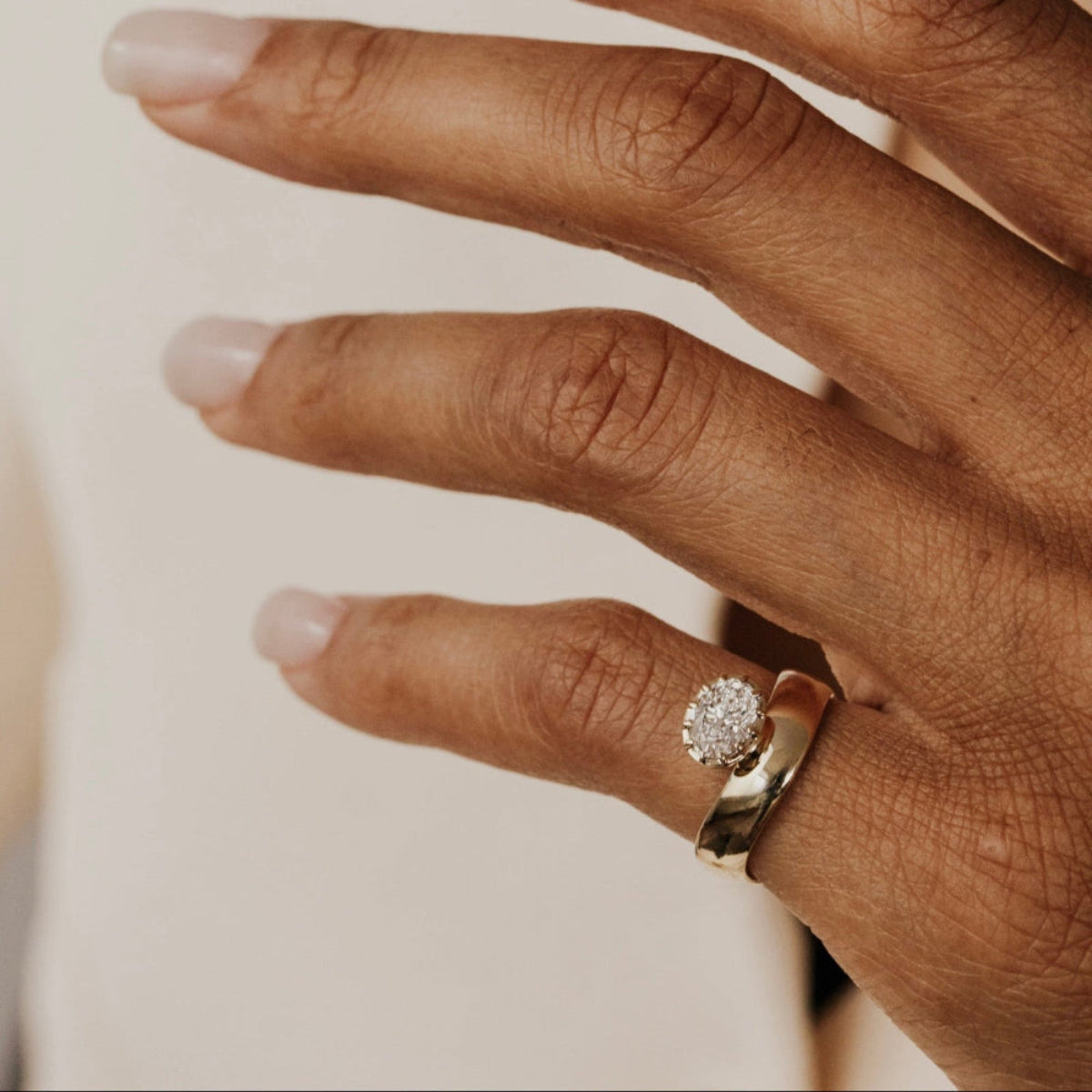 Close-up of a hand wearing the gold Reflection pinky ring with an oval lab grown diamond on a neutral background.