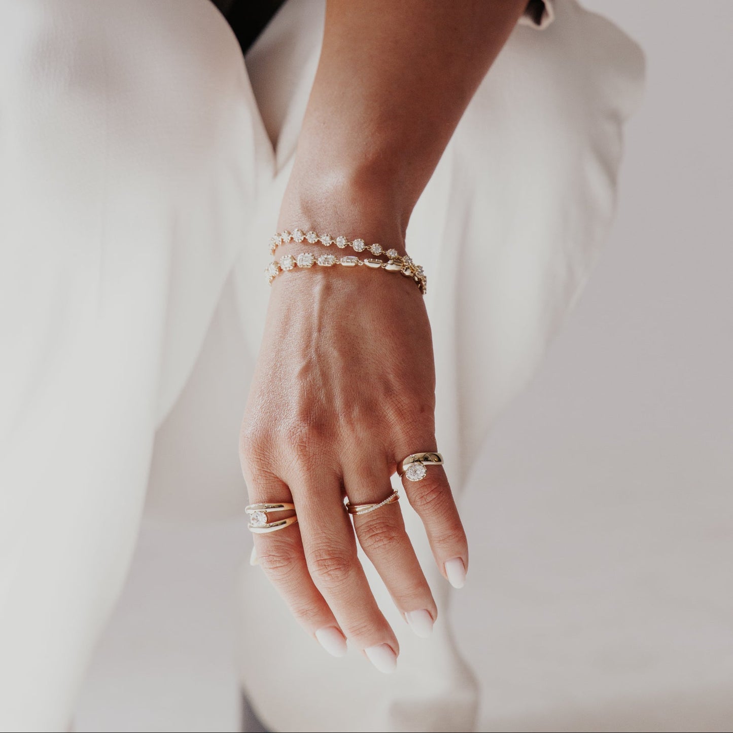 Close-up of a person's wrist with multiple lab grown diamond bracelets and ring hand diamond rings on a neutral background.