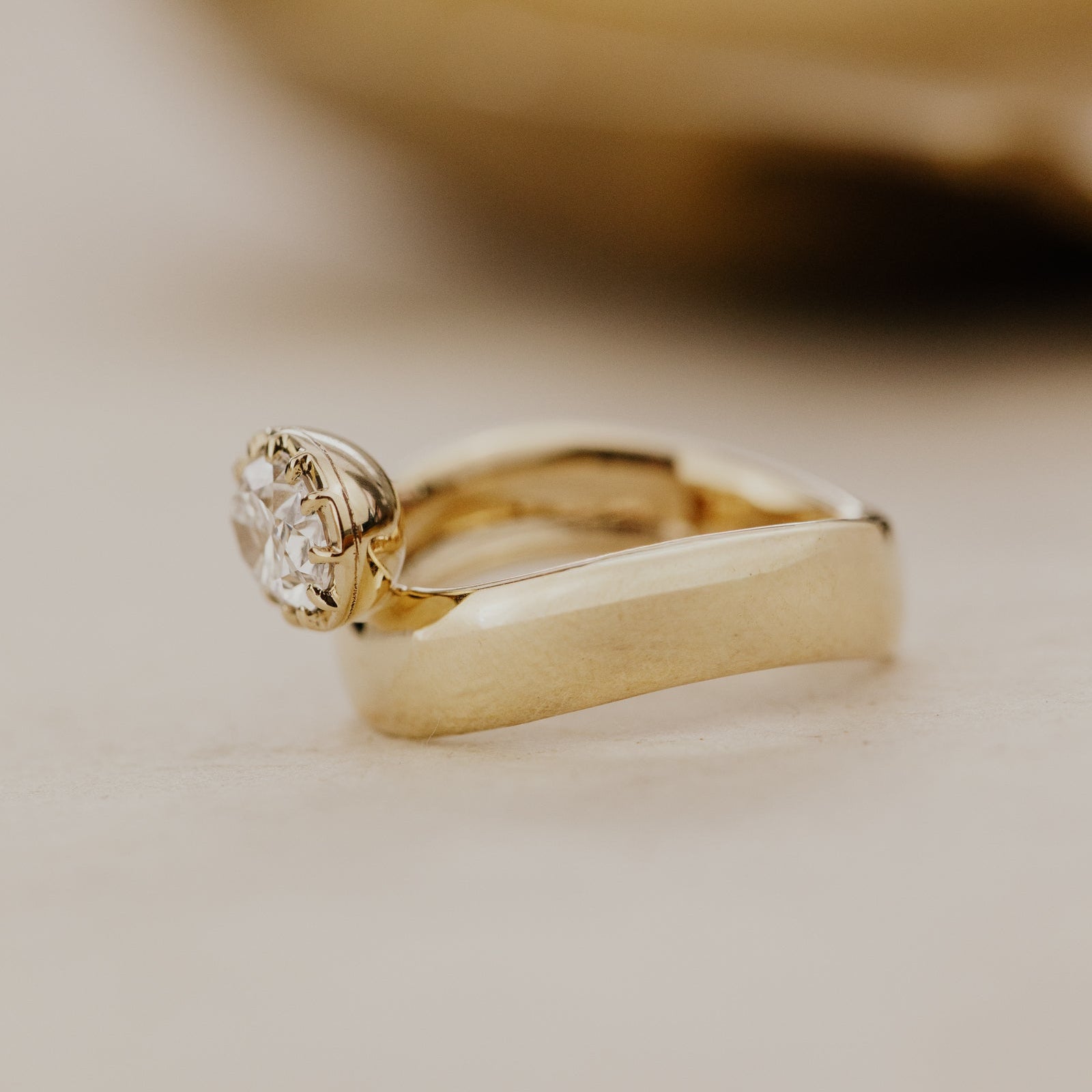Side view of the gold Reflection pinky ring with an oval lab grown diamond on a beige background.