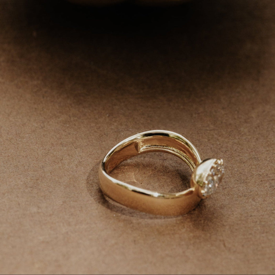 Side view of the Reflection pinky ring with an oval lab grown diamond on a brown surface.