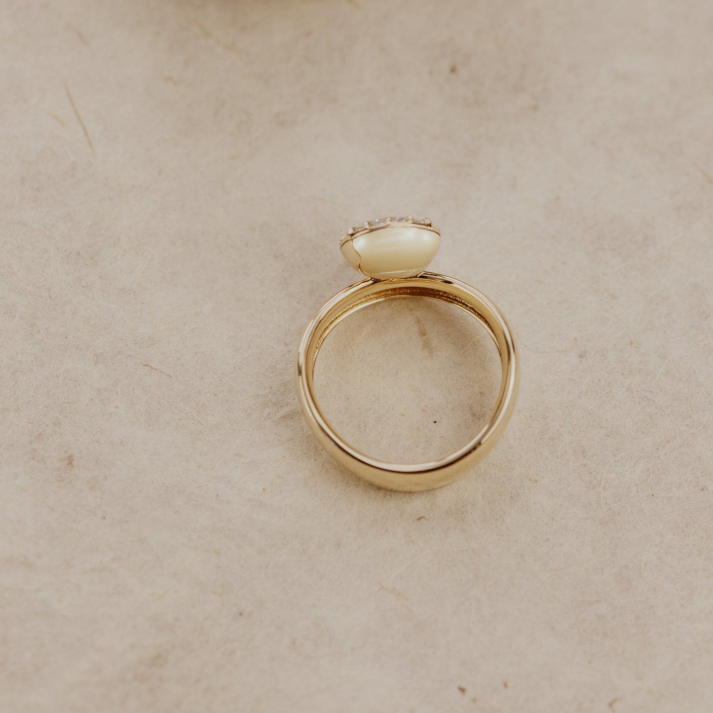 Top down view of the Reflection pinky ring with an oval lab grown diamond center stone on a beige surface.