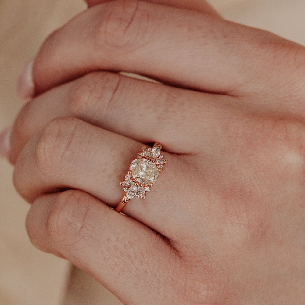 Close-up of a hand wearing a rose gold champagne diamond ring against a neutral background.