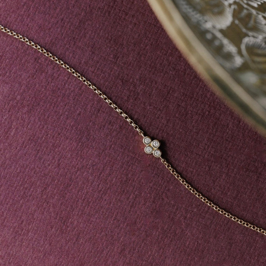 A delicate gold chain necklace with a small four-stone diamond cluster pendant, displayed on a textured dark purple surface.