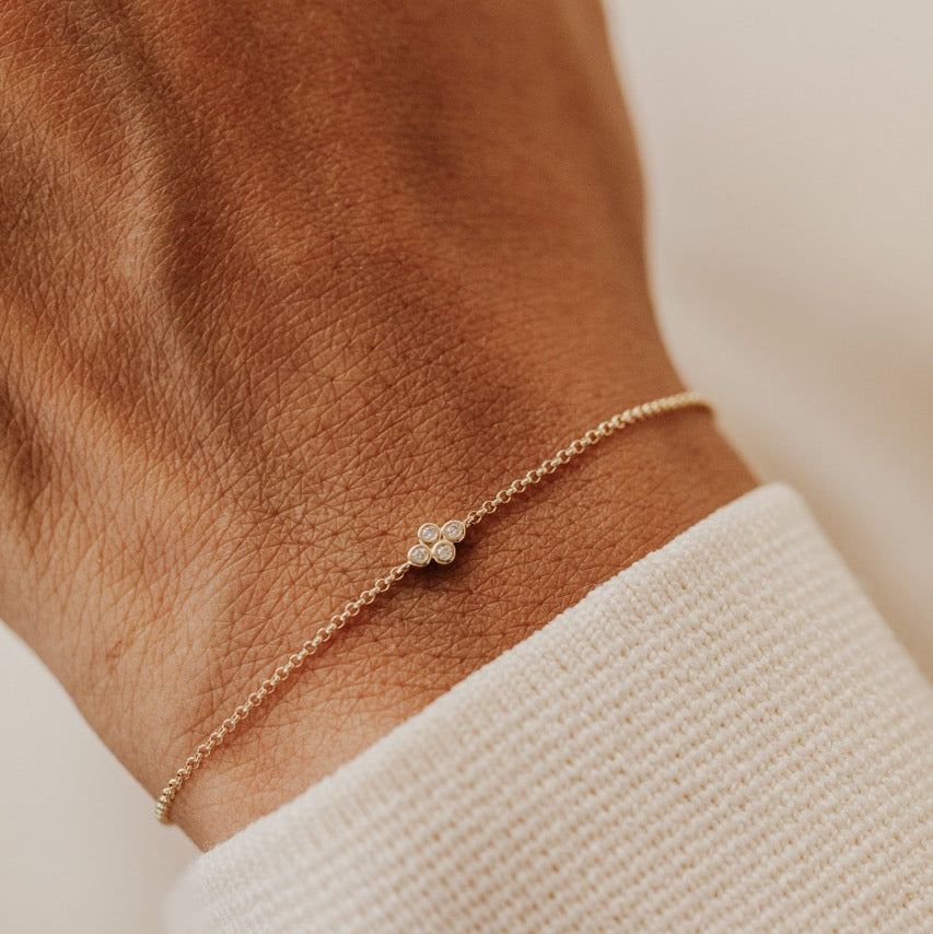 A delicate gold chain bracelet with a small diamonds cluster, shown worn on a person's wrist over a white knit cuff.