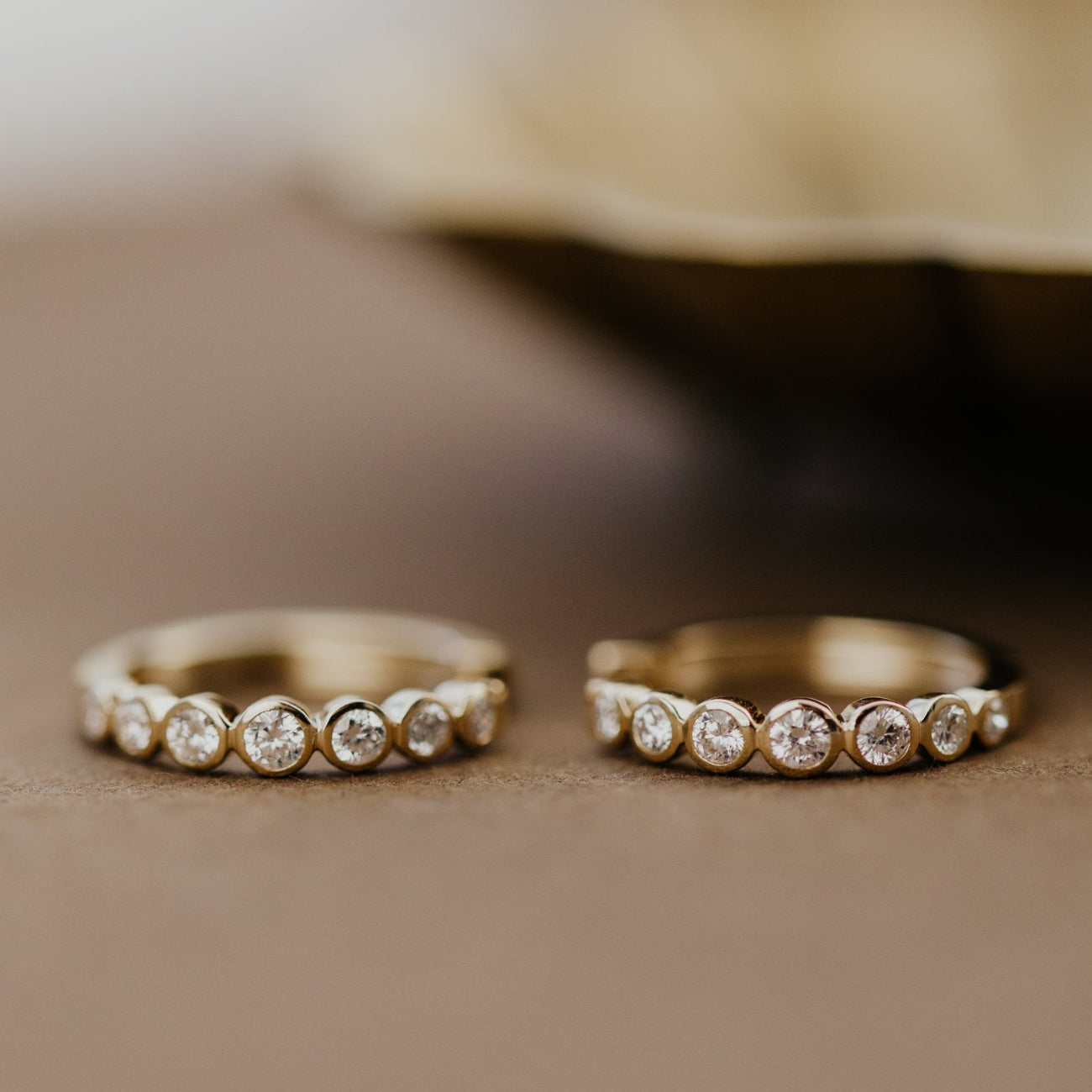 Two gold hoop earrings with diamond accents on a beige surface.