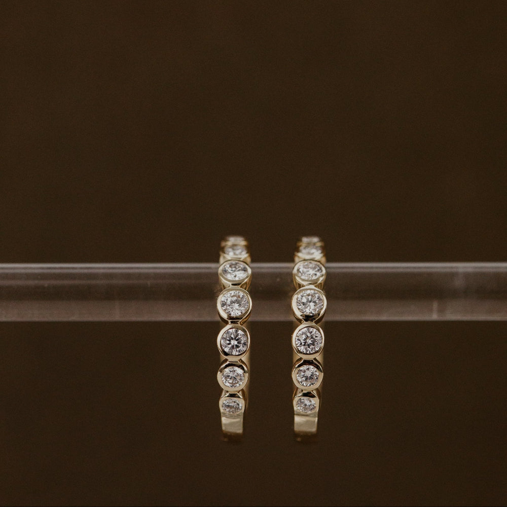Gold hoop earrings with round diamonds on a dark background.