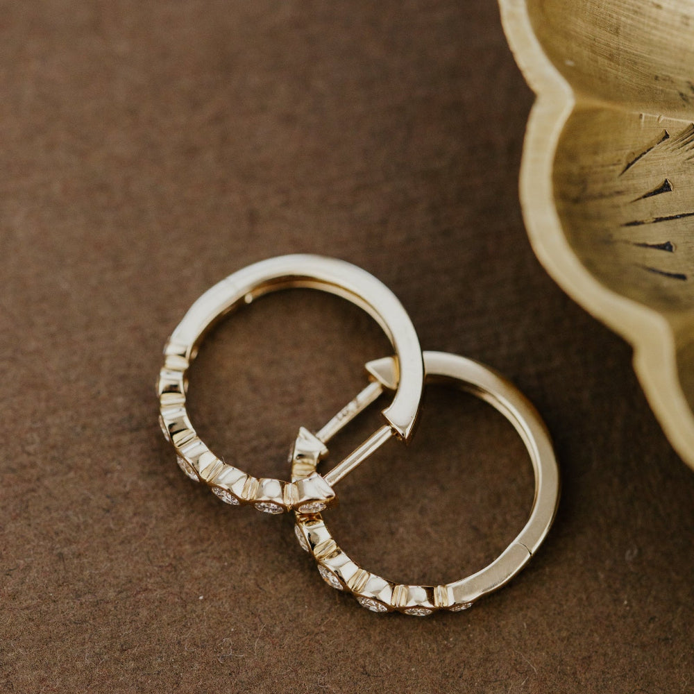 Two gold hoop earrings with diamond accents on a brown surface.