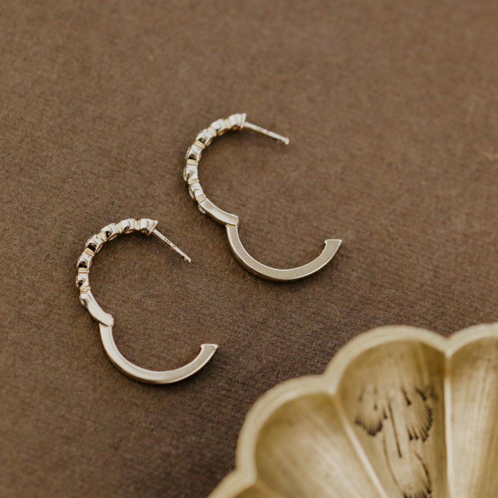 Pair of yellow gold hoop earrings on a brown surface with a gold dish.