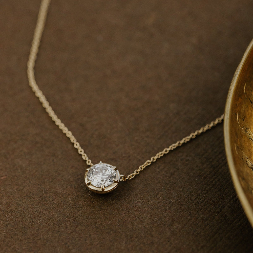 Gold necklace with a round lab grown diamond pendant on a brown textured surface.
