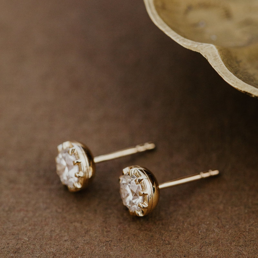 Gold lab grown diamond stud earrings on a brown surface.